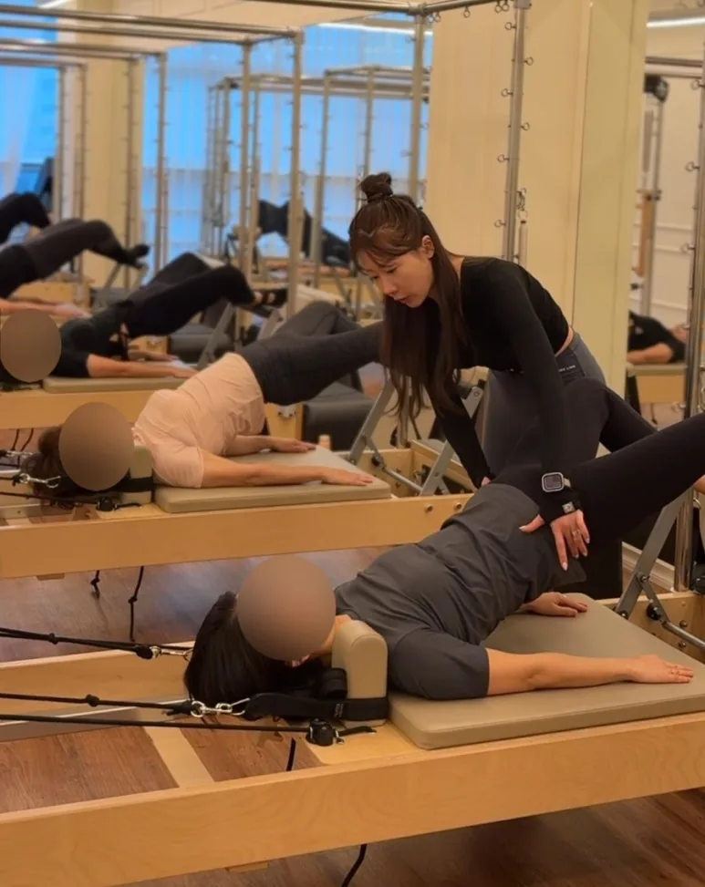 리포머 그룹수업 중 강사가 회원의 다리 움직임을 가까이에서 살펴보는 장면
